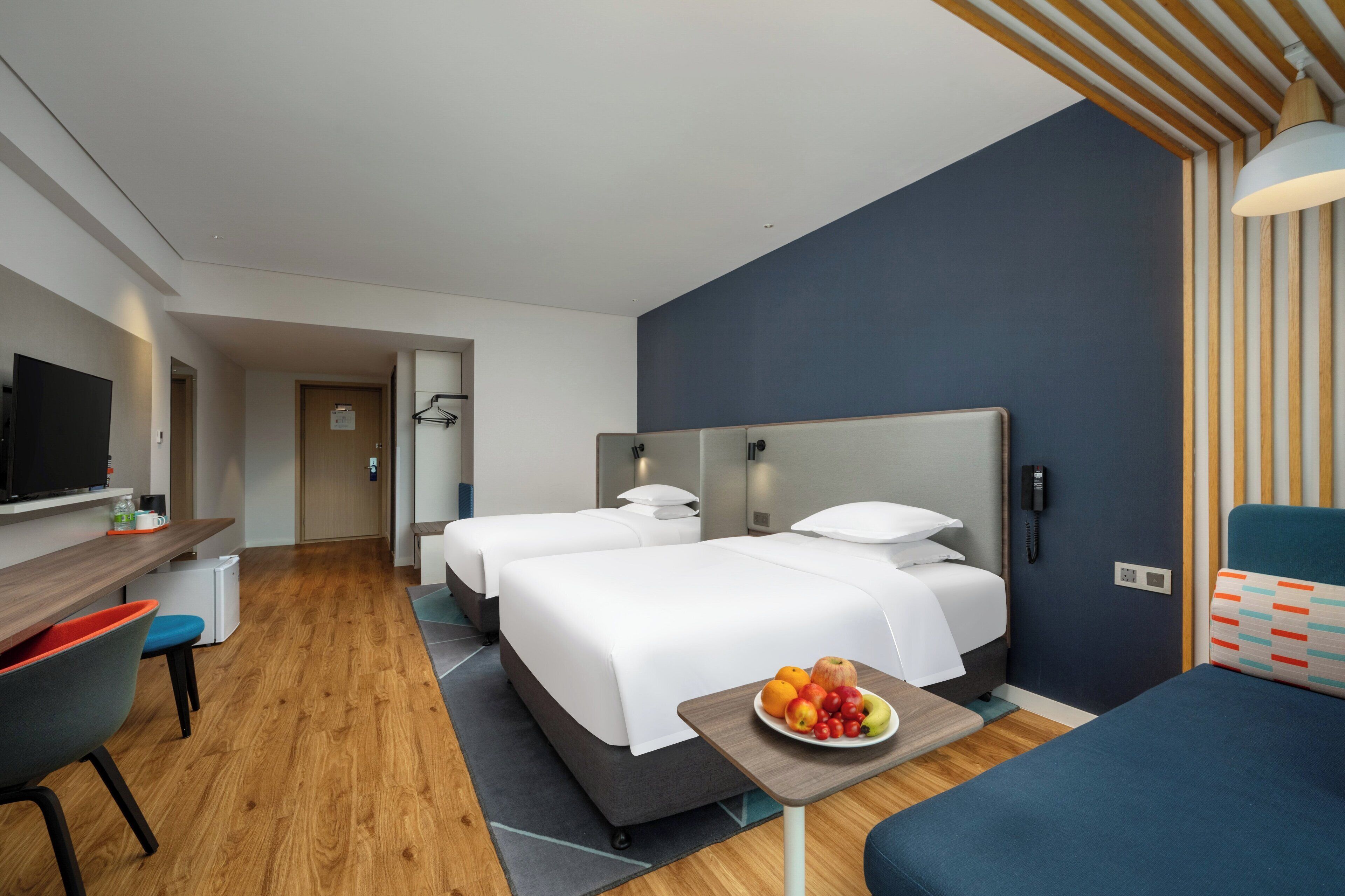 Habitación de hotel con dos camas, un escritorio, un televisor y un frutero en la mesita de noche.