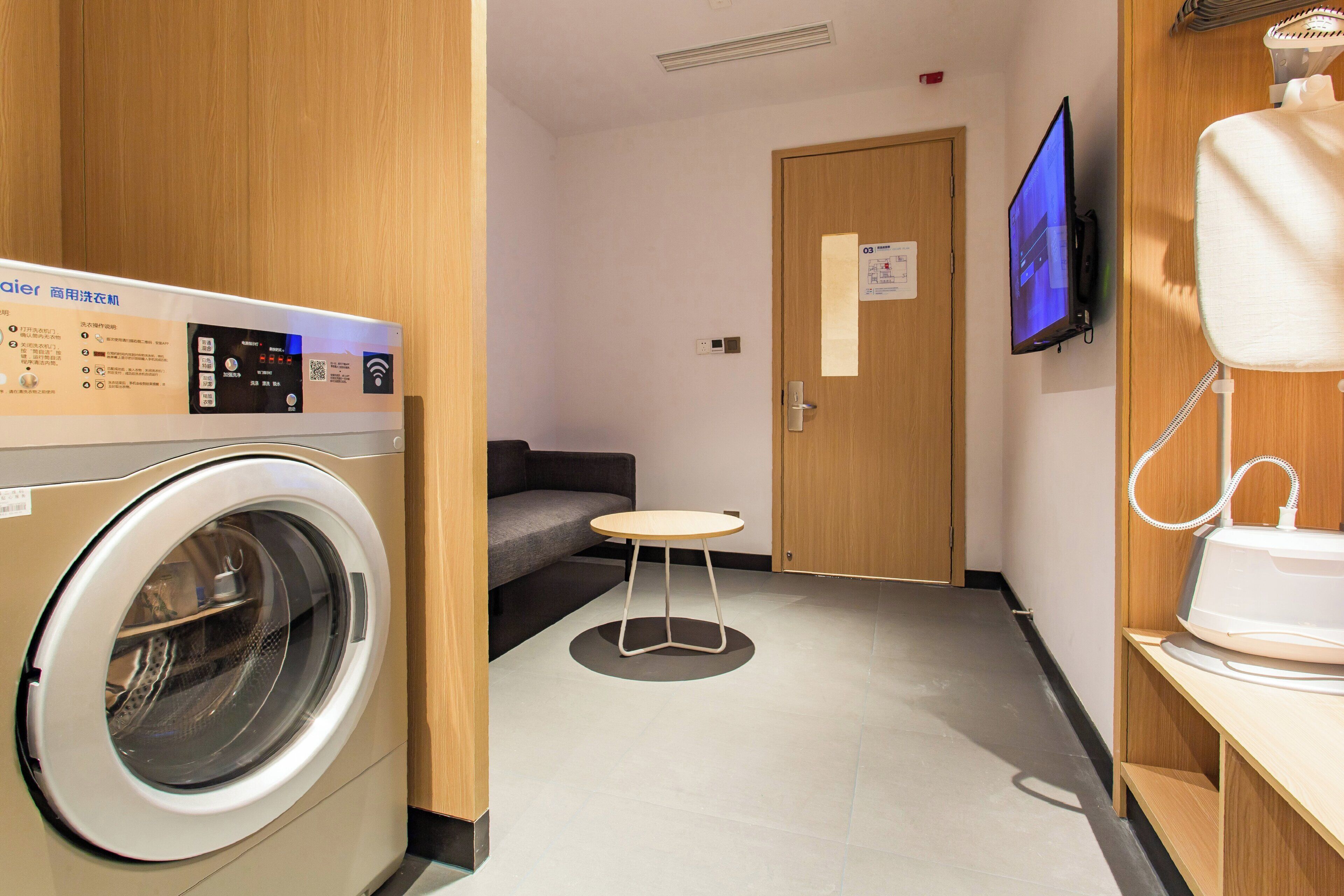 Une chambre d’hôtel équipée d’un lave-linge, d’une petite table, d’un canapé et d’une télévision.