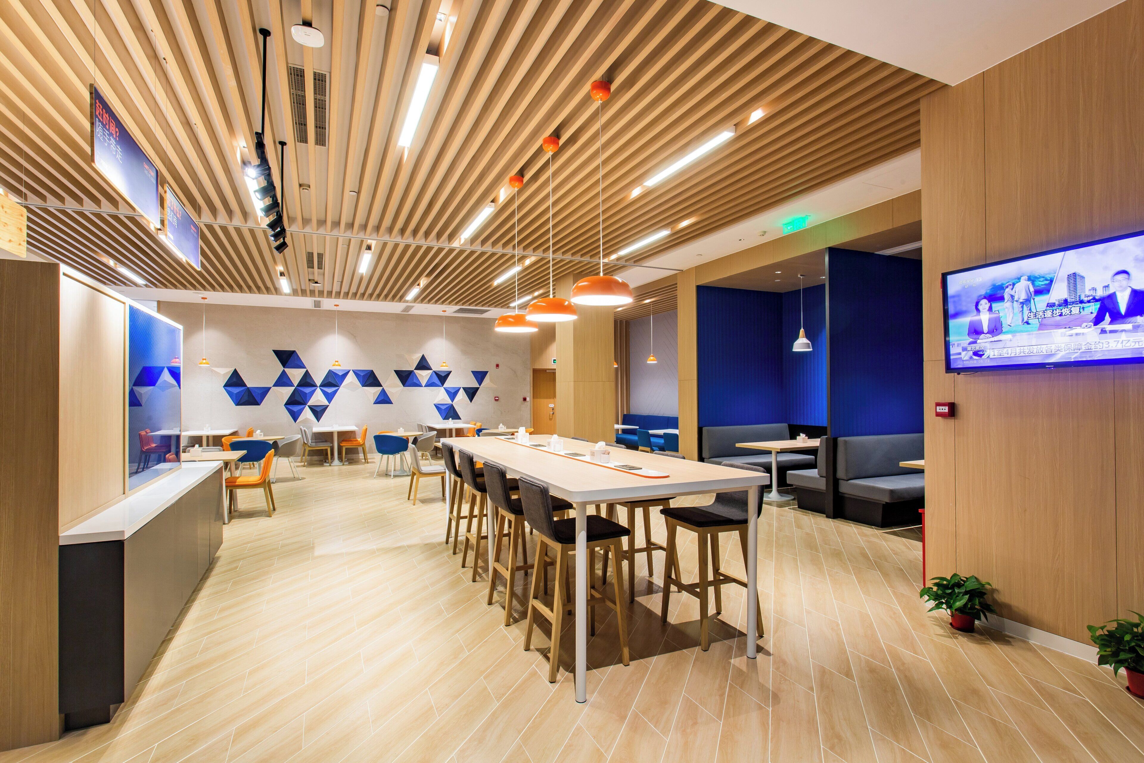 A modern interior with a long communal table, individual seating, and a television screen.