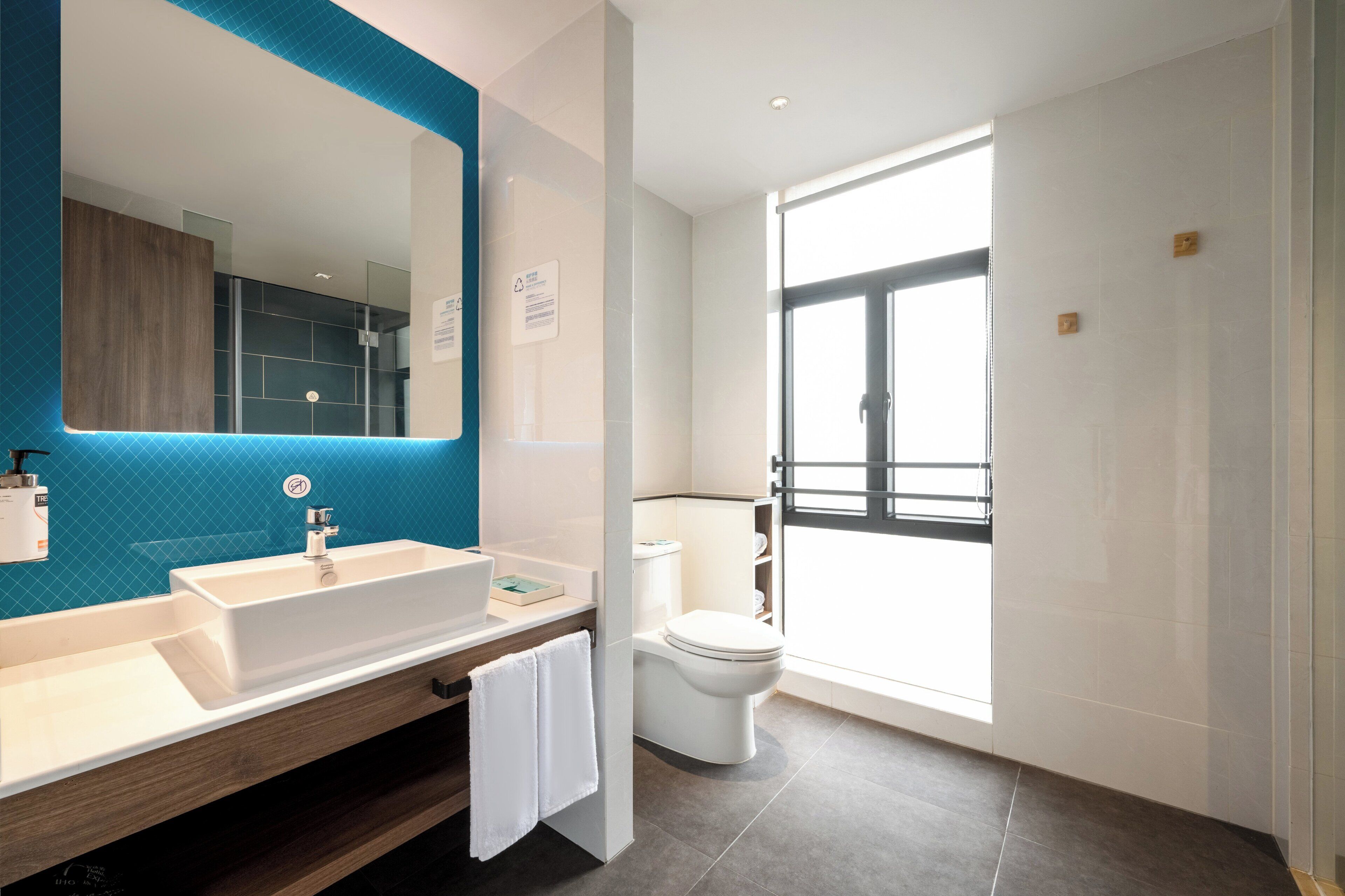 Een moderne badkamer met een grote spiegel, twee wastafels, een toilet en een douchehoek.