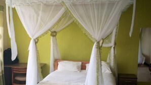 A bed with a canopy, a wooden nightstand, a chair, and a small table. - Hungry & T Hippo (Naivasha)