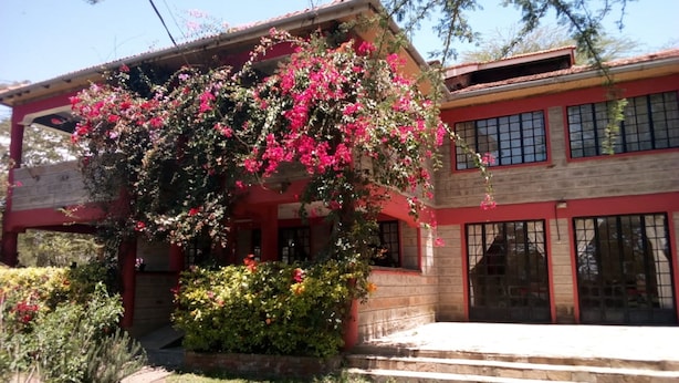 A two-story building with a red facade, large windows, and a covered porch with pink flowering plants. - Hungry & T Hippo (Naivasha)