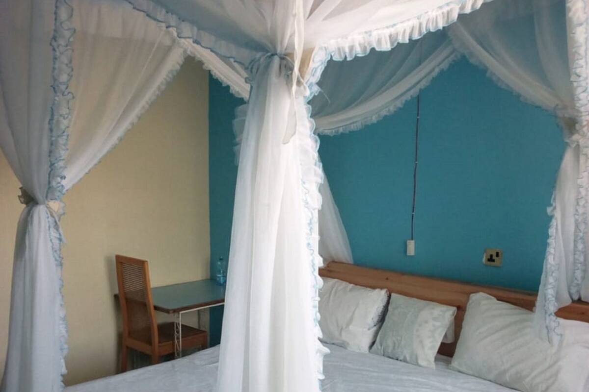 A four-poster bed with white bedding and a blue wall in the background.