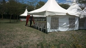 A series of white tents with a peaked roof design, arranged in a row on a grassy field with trees in the background. - Hungry & T Hippo (Naivasha)