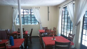 A dining area with wooden tables and chairs, white curtains, and large windows. - Hungry & T Hippo (Naivasha)