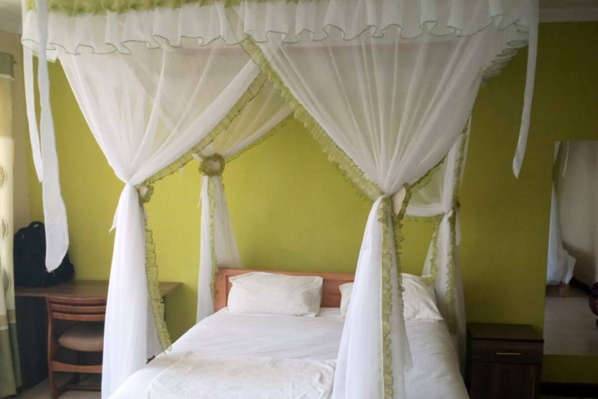 A bed with a canopy, a nightstand, and a chair in a room with green walls.