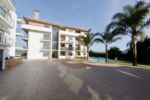 A modern multi-story building with balconies, a swimming pool, and palm trees. - Vela - Excellent 3 bedroom apartment in a popular complex - close to the beach (São Martinho do Porto)