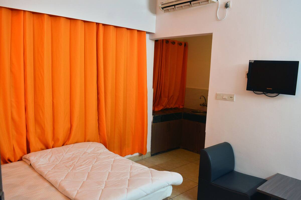 Une pièce avec un lit, une chaise, un téléviseur et une porte de salle de bain entrouverte.