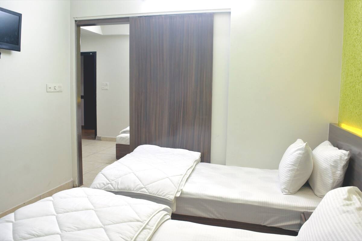 Une chambre d’hôtel avec deux lits, une porte coulissante et un téléviseur fixé au mur.