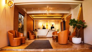 Un hall d’hôtel avec un comptoir d’accueil, deux réceptionnistes et un escalier menant à l’étage supérieur.