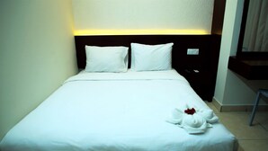 Un lit bien fait, avec du linge de lit blanc et des oreillers, une table de chevet avec un téléphone et un luminaire fixé au mur.