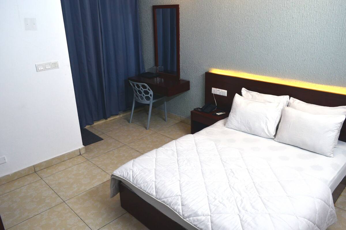 Une chambre d’hôtel comprenant un lit, un bureau, une chaise, un miroir et une table de chevet avec une lampe.
