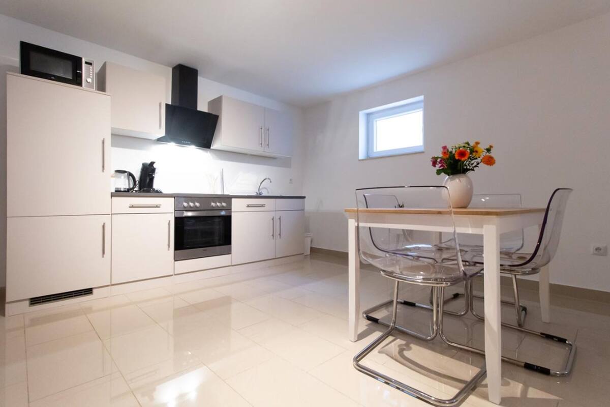 A modern kitchen with white cabinets, a stainless steel oven, and a dining area with a clear glass table and chairs.