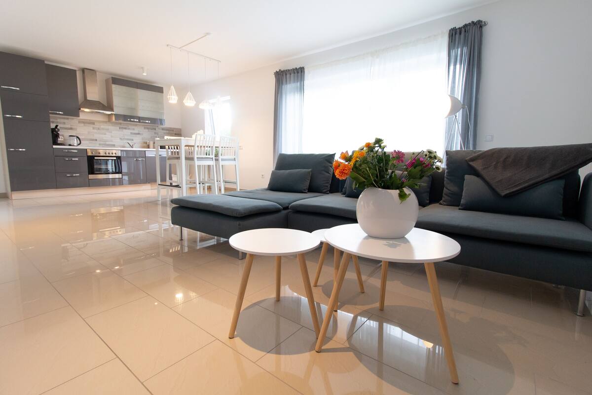 A modern living room with a grey sofa, two white round tables, and a vase of flowers.