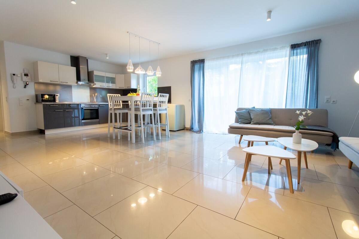 A modern kitchen with white cabinets, a dining area with a white table and chairs, and a living area with a sofa and a small coffee table.