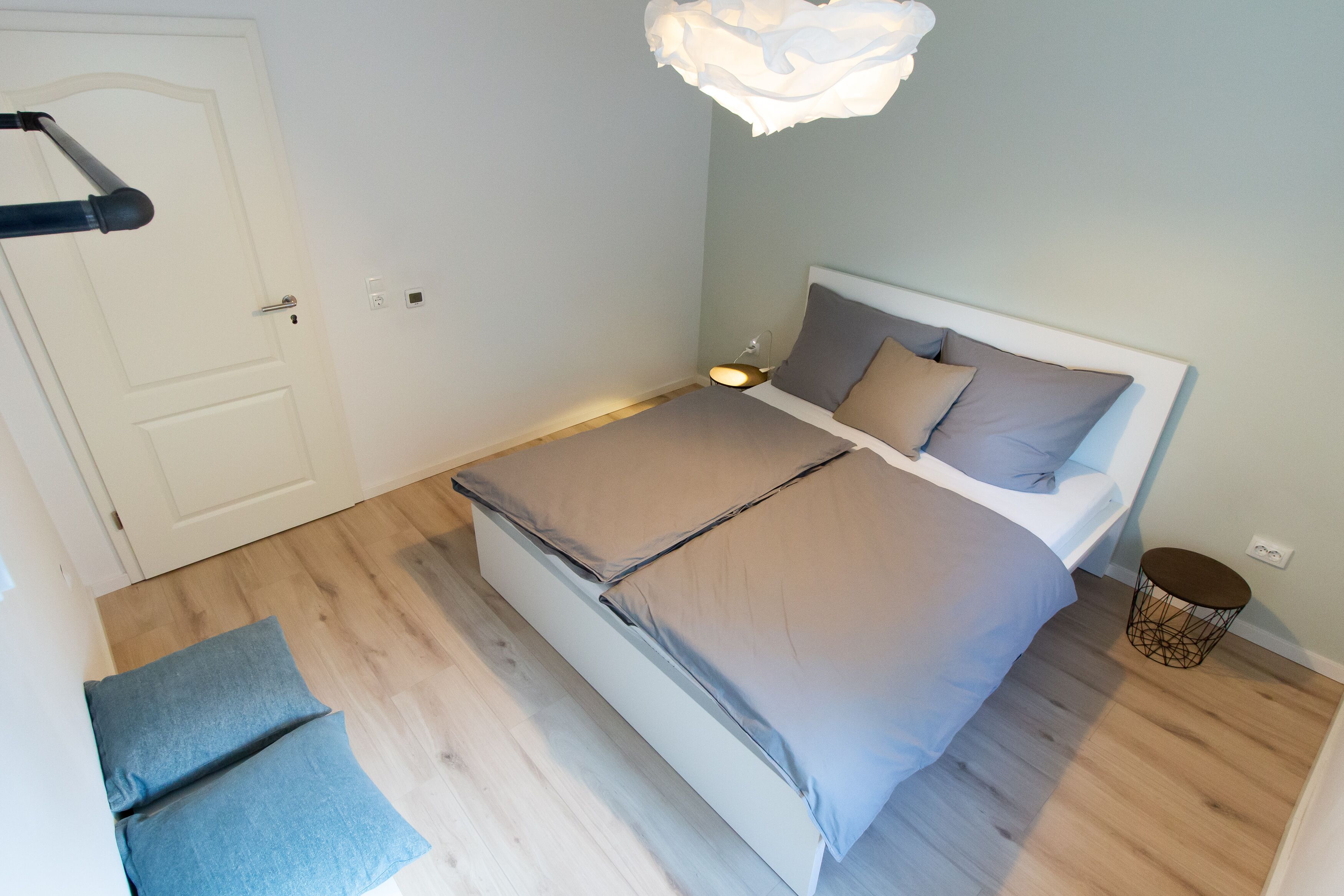 A bedroom with a bed, bedside table, lamp, and a small round stool.
