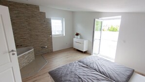 A modern bedroom with a large bed, a small white dresser, a window, and a door leading to a balcony. - T & T Suites Raunheim (Raunheim)