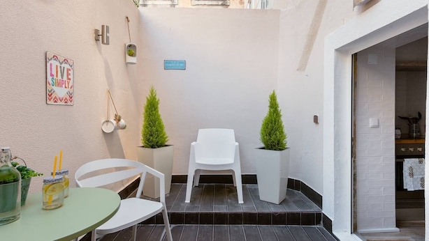 Un espacio exterior pequeño y cerrado con una mesa, sillas, plantas en macetas y un letrero en la pared.