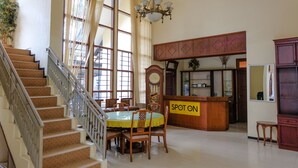 Un vestíbulo amplio con una escalera, una mesa redonda para comer con sillas, un mostrador de recepción de madera y un reloj grande.