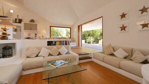 A modern living room with a glass coffee table, beige sofas, and a bookshelf. - Beautiful private villa for 7 people with WIFI, TV, terrace and pets allowed (Aglientu)