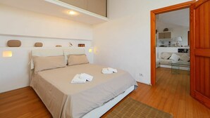 A bedroom with a bed, a wooden floor, a small rug, and a wooden door leading to another room. - Beautiful private villa for 7 people with WIFI, TV, terrace and pets allowed (Aglientu)