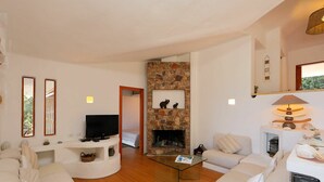 A modern living room with a stone fireplace, a television, and a sofa. - Beautiful private villa for 7 people with WIFI, TV, terrace and pets allowed (Aglientu)