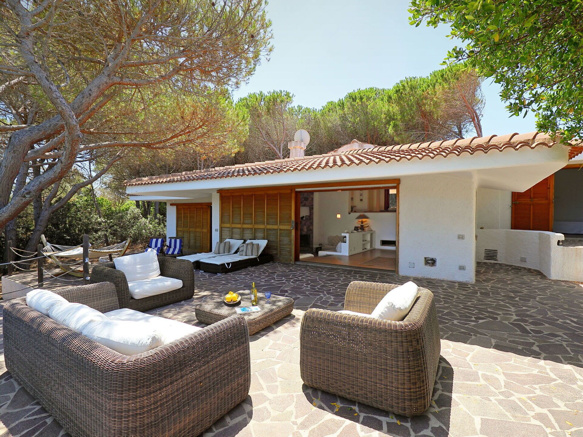 A modern villa with a stone patio, wicker furniture, and a glass door leading to a kitchen.