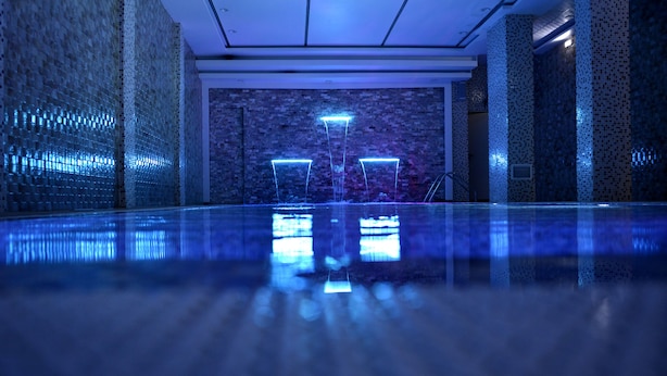 A modern indoor pool area with a reflective floor, a brick wall, and three illuminated columns. - Hotel Amsterdam (Algiers)