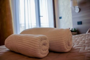 A neatly made bed with two rolled towels placed on it.