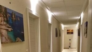 Ein Flur mit Türen links, einem Bild an der Wand und einem gefliesten Boden.