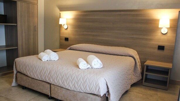 Ein Hotelzimmer mit einem großen Bett, zwei Wandlampen, einem Holzkopfteil und einem kleinen Nachttisch.
