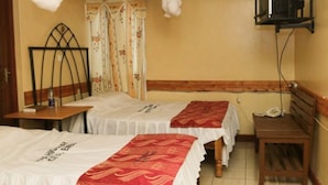A hotel room with two beds, a wooden nightstand, a small table, a telephone, and a curtain with floral patterns. - Maina Highway Hotel (Embu)