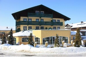 A multi-story building with a yellow facade and green balconies, surrounded by snow.