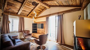 A cozy living room with a wooden ceiling, a sofa, a chair, a TV, and a fireplace. - Posthotel Rattenberg (Rattenberg)