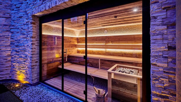 A spa area with wooden walls and a glass door, featuring a bench and a small table with a bucket. - Posthotel Rattenberg (Rattenberg)