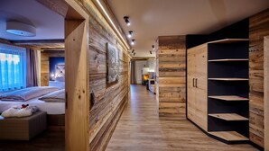 A modern hotel room with a wooden floor, a bed with white bedding, a wooden wardrobe, and a hallway with wooden walls and ceiling. - Posthotel Rattenberg (Rattenberg)