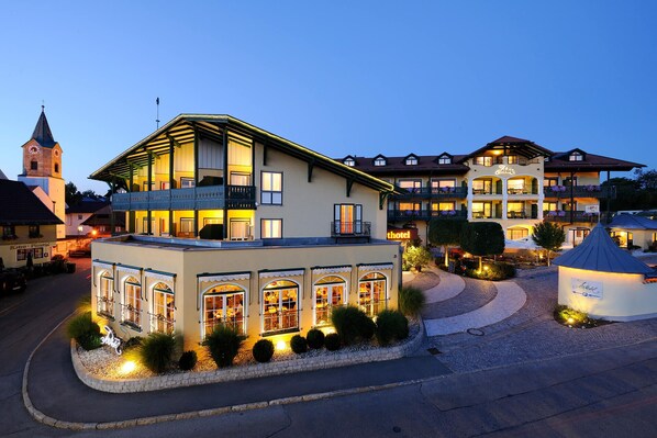 A hotel with a prominent balcony, a clock tower in the background, and a well-lit entrance.