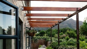 A covered outdoor patio with metal chairs and tables, a brick wall, and a view of a mountainous landscape. - Vineyard Views Country House (Riebeek Kasteel)