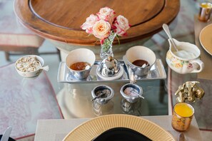 En morgenmadsopstilling med en bakke, skåle med mad, en vase med blomster og en dekorativ ske.