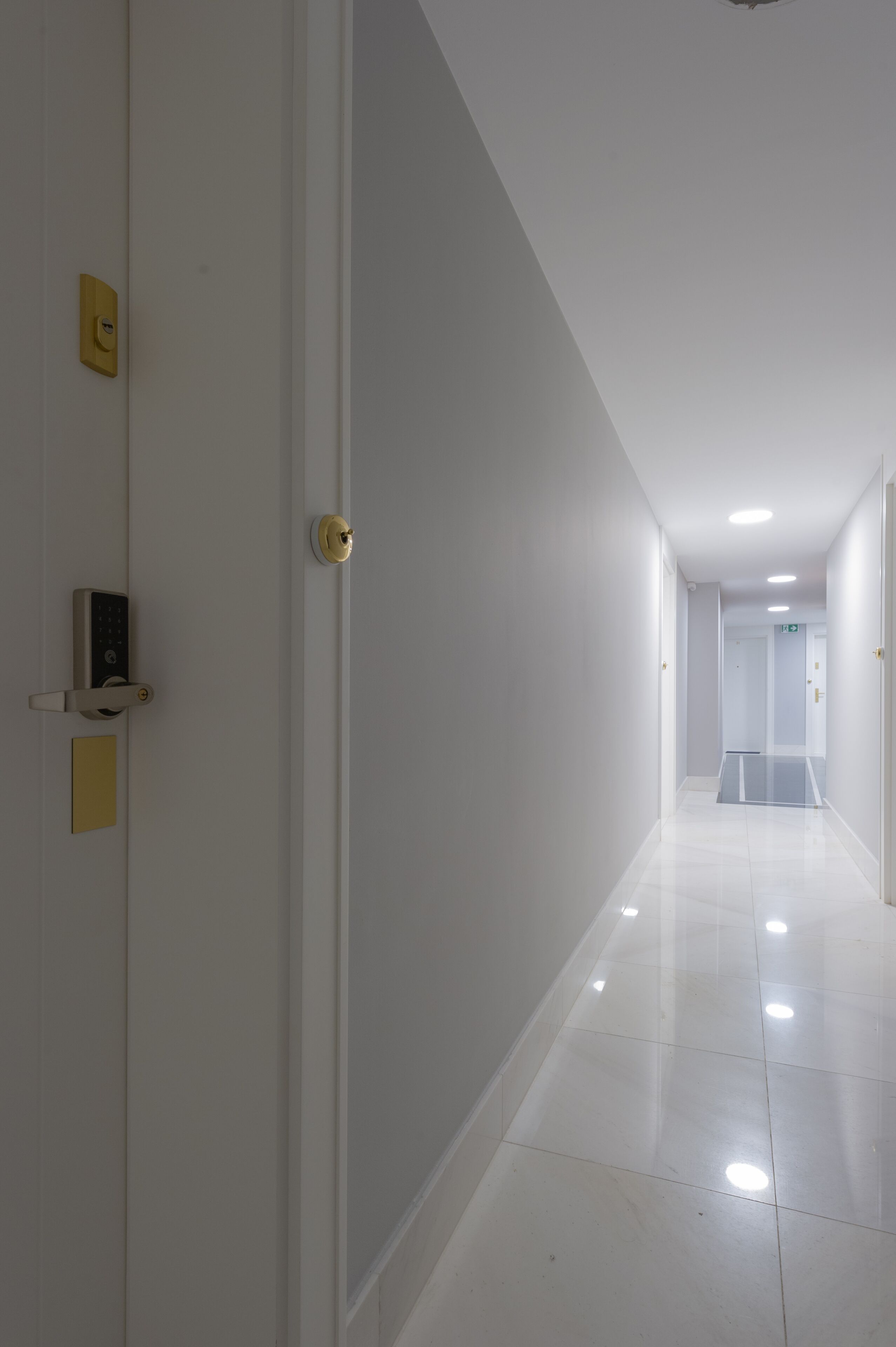 Corredor limpo e moderno, com uma porta à esquerda, uma fechadura eletrônica e um interruptor de luz na parede.
