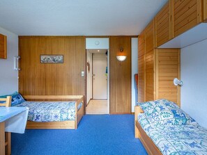 A room with two wooden beds with patterned bedding, a desk, and a wardrobe.