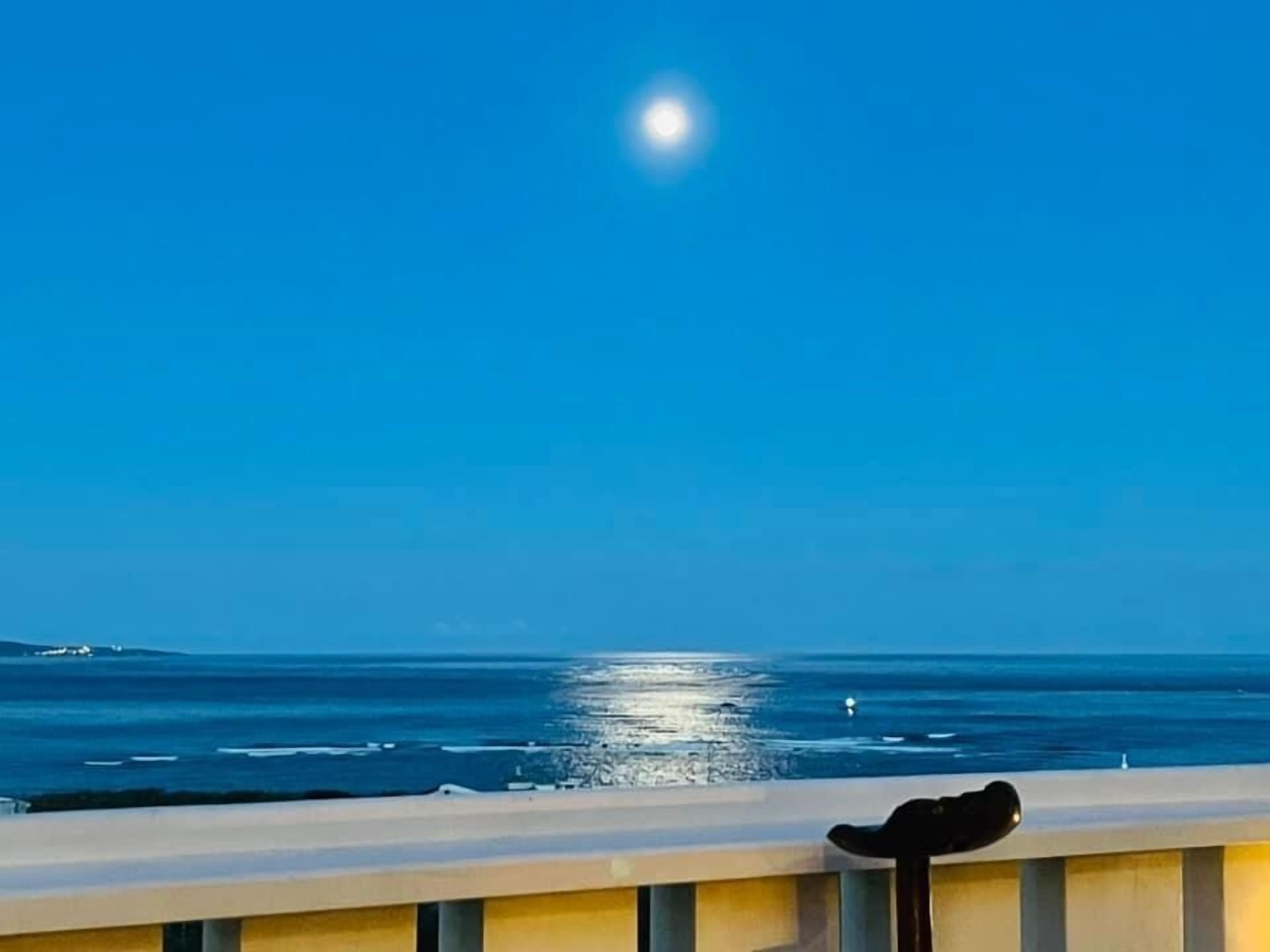 Un balcon avec vue sur l’océan et une lune dans le ciel.