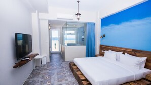 Quarto com uma cama grande, televisão e vista para o mar através de uma porta de vidro.