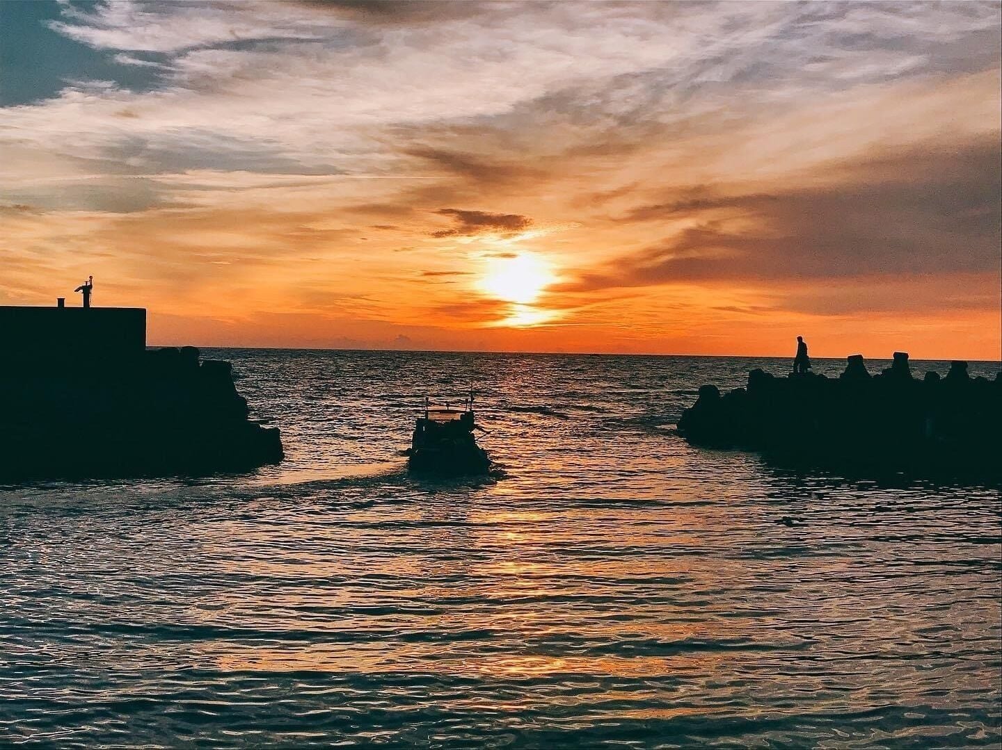 A sunset over a calm sea with a pier extending into the water.