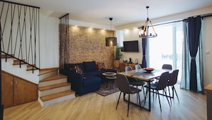 A modern living space with a staircase, a blue sofa, a dining table with chairs, and a brick wall. - Villa Marghareta 2 (Dubrovnik)