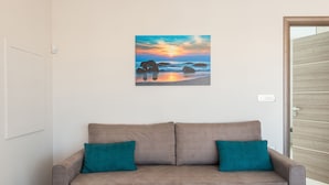 A beige sofa with teal cushions, a framed landscape painting, and a wooden door. - Mimosa Cozy & Modern Flat steps from Sandy Beach (Platanias)
