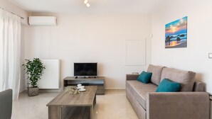A modern living room with a sofa, a coffee table, a TV, a potted plant, and a painting on the wall. - Mimosa Cozy & Modern Flat steps from Sandy Beach (Platanias)