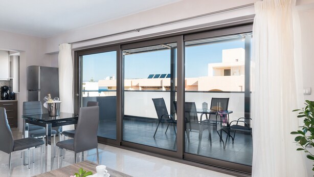 A modern kitchen with a refrigerator, a dining area with a glass table and chairs, and a balcony with chairs and a table. - Mimosa Cozy & Modern Flat steps from Sandy Beach (Platanias)