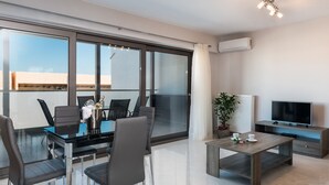 A modern living room with a glass partition, a flat-screen TV, a coffee table, and a dining area with chairs and a table. - Mimosa Cozy & Modern Flat steps from Sandy Beach (Platanias)
