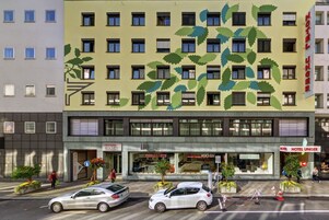 Un hotel con fachada verde y motivos de hojas, con varias ventanas y un letrero que dice 'Hotel Unger'.